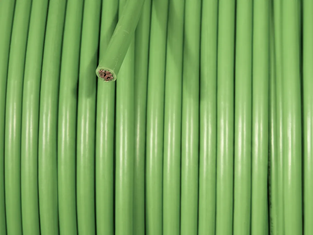 Green cable coiled tight on a spool, one end cut to show the copper conductors